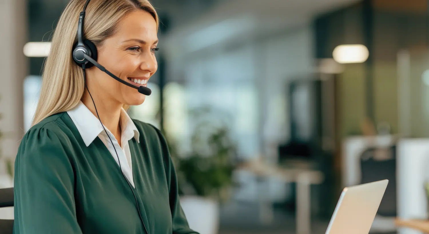 GMY Nahaufnahme einer lächelnden Kundendienstmitarbeiterin, die am Schreibtisch mit Laptop arbeitet.